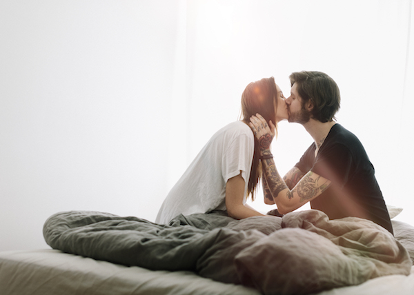 young couple finds time to stay committed while kissing in bed